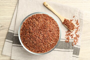 Brown rice in glass bowl and spoon on wooden table, flat lay