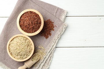 Different types of brown rice in bowls and scoop on white wooden table, flat lay. Space for text