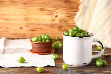 Cup and bowl with fresh gooseberries on wooden background