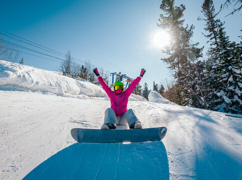 Snowboarder enjoys a sunny day on the slopes with arms raised in excitement at a winter resort