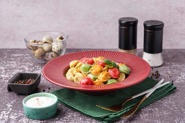 Plate of boiled colorful dumplings with basil and bowl of sour cream on dark table