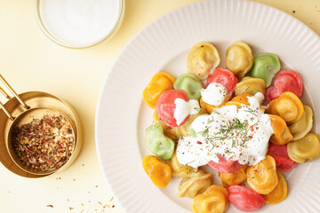 Plate of boiled colorful dumplings with sour cream and dill on yellow background