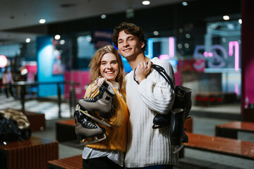 Young couple smiling while holding ice skates in a rink at night
