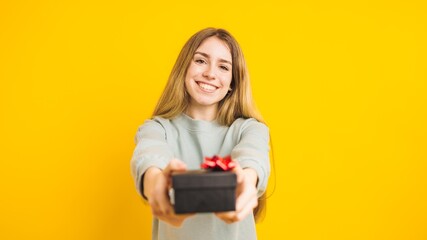Naklejka premium Young woman giving a gift on yellow background