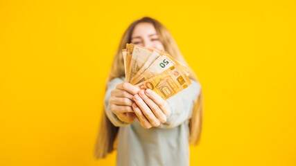 Young woman showing euro banknotes on yellow background