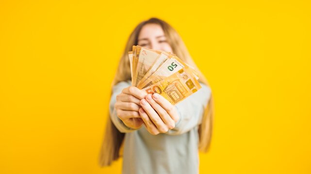Young woman showing euro banknotes on yellow background