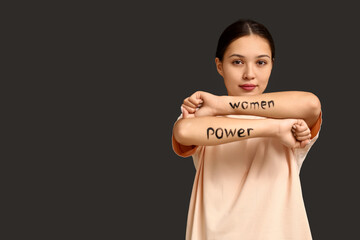 Young woman with words WOMEN POWER written on her arms against black background. Feminism concept