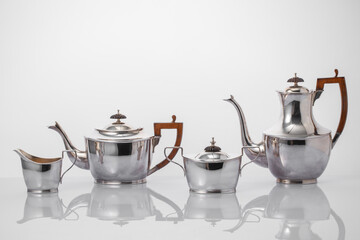 silver coffee pot, milk jug, sugar bowl and teapot set on white background with reflection