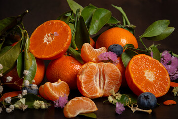 Close-up of cut oranges and tangerines with flowers and green leaves, on wood, horizontal