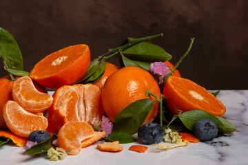 Close-up of oranges and tangerines with flowers and green leaves, on white marble, horizontal, with copy space