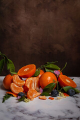 View of cut oranges and tangerines with flowers and green leaves, on white marble, vertically, with copy space
