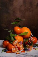 Top view of oranges and tangerines in a pile with flowers and leaves, on white marble, vertical, with copy space