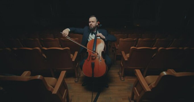 A cellist plays classical music in an empty, dark hall of an ancient theater.