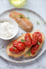 Roasted tomato bruschettas with stracciatella or stretched curd cheese served on a grey plate, vertical shot, middle close-up