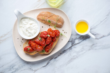 Stracciatella cheese with roasted tomato bruschettas on a beige plate, horizontal shot on a white granite background, flat lay