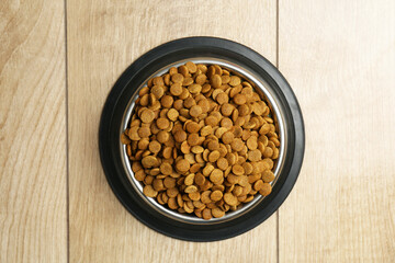 Dry pet food in feeding bowl on wooden floor, top view