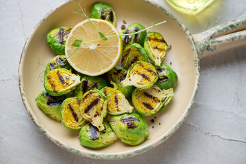 Beige serving pan with roasted Brussels sprouts and lemon, horizontal shot, middle closeup