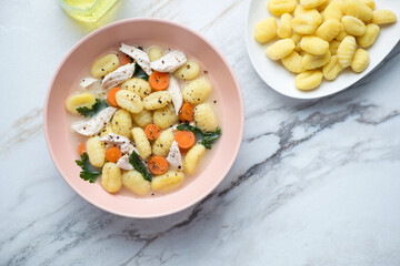 Roseate plate with creamy chicken gnocchi soup, horizontal shot on a white granite background with space, flat lay