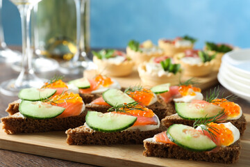 Tasty canapes with salmon and cucumber on wooden table, closeup