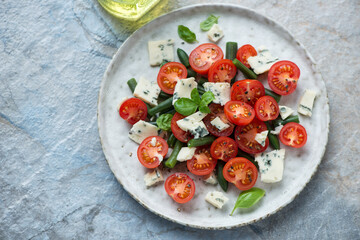 Salad with cherry tomatoes, green beans and blue cheese, horizontal shot on a blue and beige stone background, high angle view