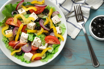 Delicious fresh Greek salad served on light blue wooden table, flat lay