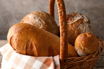 Different freshly baked bread loafs in wicker basket on table, closeup