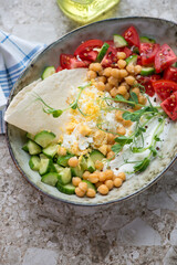 Yogurt bowl with vegetables, chickpeas, grated egg and flatbread, vertical shot on a light-brown granite background, middle closeup
