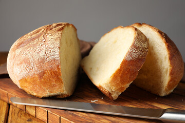 Cut loaf of fresh bread and knife on wooden table, closeup