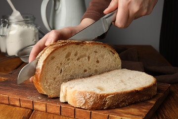 Woman cutting freshly baked bread at wooden table, closeup