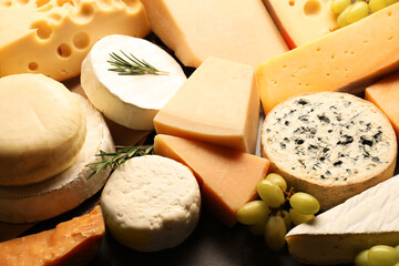 Different types of cheese, rosemary and grapes on table, closeup