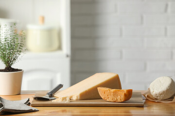 Different types of cheese, slicer and potted thyme on wooden table indoors. Space for text