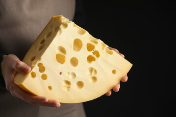 Woman with piece of delicious cheese on black background, closeup