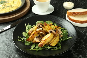 Tasty brunch. Delicious fried potatoes with arugula and mushrooms served on black textured table, closeup
