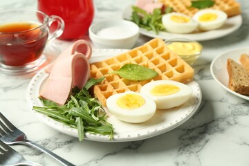Tasty brunch. Boiled egg, Belgian waffle, arugula and ham on white marble table, closeup