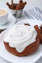 Tasty cinnamon roll with cream, spices and coffee on white table, closeup