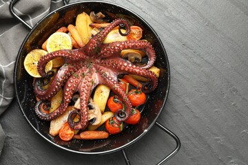 Fried octopus with mushrooms, lemon and vegetables on grey textured table, top view. Space for text