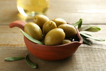 Tasty green olives and leaves in bowl on wooden table, closeup