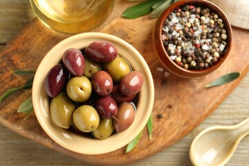 Tasty olives in bowl, leaves and spices on wooden table, flat lay