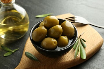 Delicious marinated olives in bowl, green leaves and oil on black table, closeup