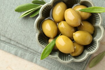 Delicious marinated olives in bowl and green leaves on grey table, top view. Space for text