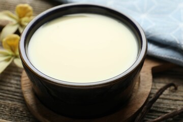 Tasty condensed milk, vanilla pods and flowers on wooden table, closeup