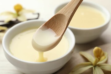 Taking tasty vanilla condensed milk with spoon from bowl on white table, closeup