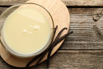Tasty condensed milk and vanilla pods on wooden table, flat lay. Space for text