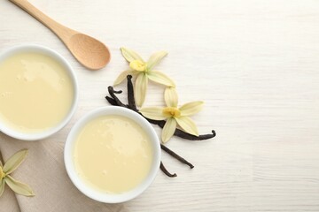 Tasty condensed milk, vanilla pods, flowers and spoon on white wooden table, flat lay. Space for text