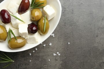 Marinated olives with feta cheese, salt and rosemary on grey table, top view. Space for text
