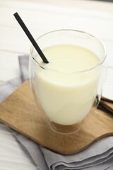 Delicious vanilla milk in glass and pods on white wooden table, closeup