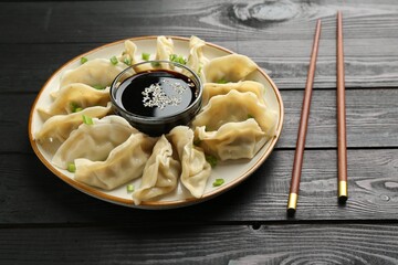 Tasty boiled gyoza (dumplings) with green onion served on black wooden table