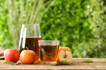 Glass and jug of fresh apple juice on wooden table outdoors