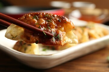 Taking tasty fried gyoza (dumpling) with chopsticks on wooden table, closeup