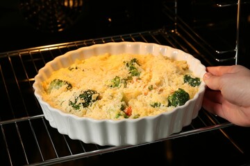 Woman putting uncooked vegetable casserole into oven, closeup